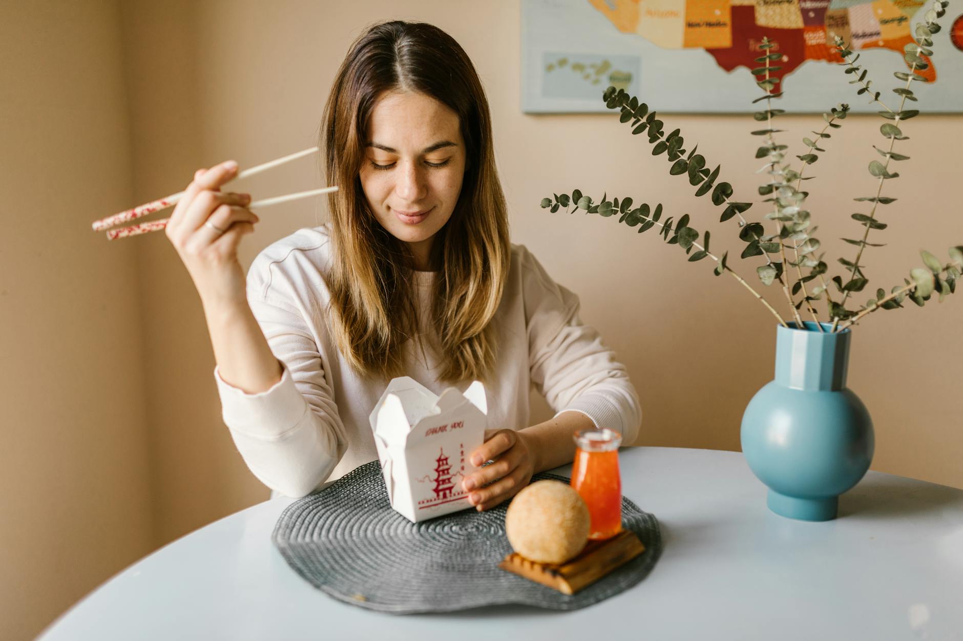 Młoda kobieta je azjatycki posiłek z pudełka pałeczkami w domu