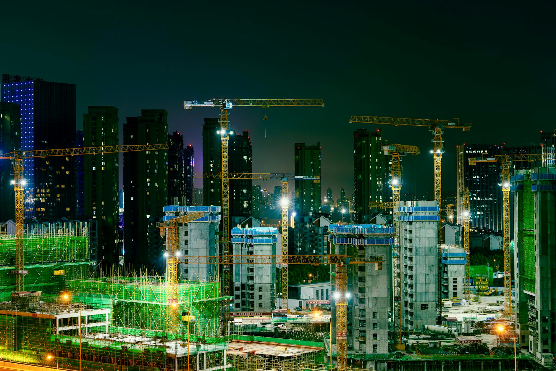 Nocny plac budowy wieżowców w mieście z dźwigami na horyzoncie