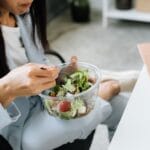 Kobieta je sałatkę warzywną przy biurku w pracy zdalnej