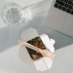 Sałatka w pudełku obok laptopa i szklanki wody, widok z góry